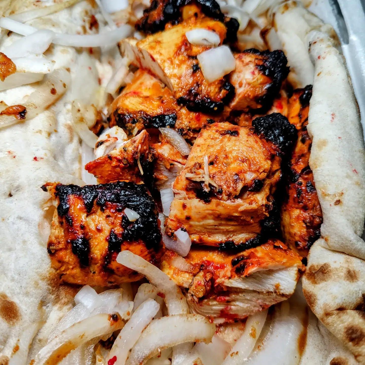  - A large Bbq chicken kebab with onions and a tub of sauce on the side.